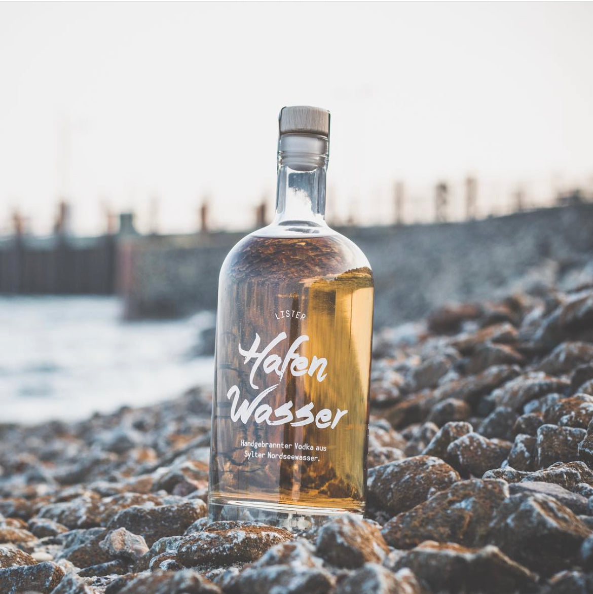 Eine Glasflasche vom Lister Hafenwasser mit dem Lister Hafen auf Sylt, im Hintergrund